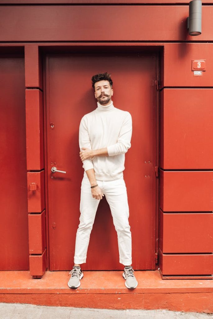 Full body of male model in monochrome white outfit standing in doorway and looking at camera